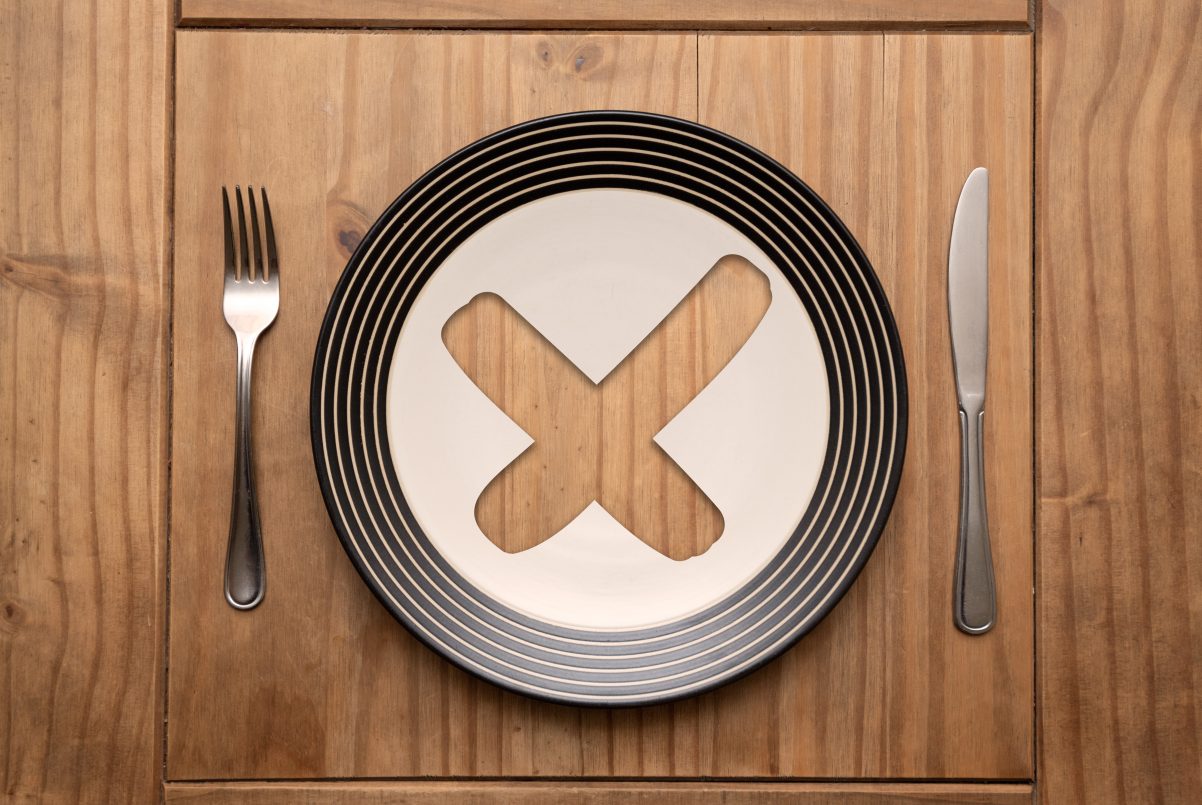 Cross mark on plate with fork and knife on rustic wooden table in natural light, top view